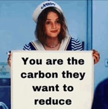 a woman in a sailor outfit is holding a sign that says you are the carbon they want to reduce