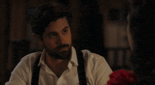a man with a beard wearing suspenders looks at a woman