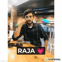 a young man sitting at a table with a sign that says raja