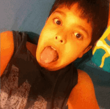 a young boy sticking his tongue out and wearing a black tank top