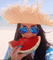 a woman wearing sunglasses and a straw hat is eating a slice of watermelon