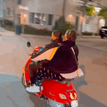 a man and a woman are riding a red scooter down a city street .