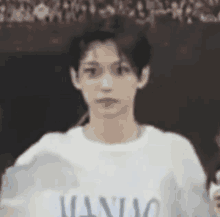 a young man is wearing a white t-shirt with the word maniac on it .