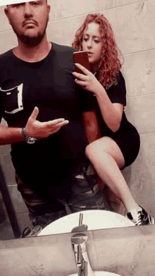 a man and a woman are taking a selfie in front of a bathroom sink