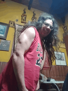 a man with long hair and glasses wears a red tank top with the number 23 on it