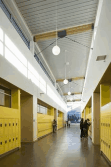 a long hallway with yellow lockers in a school with people walking down it .