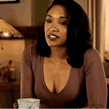 a woman is sitting at a table holding a cup of coffee and wearing a very plunging neckline sweater .