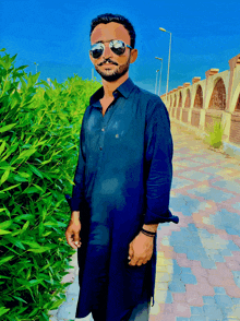 a man wearing sunglasses and a black shirt is standing in front of a bush