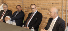 a group of men sit at a table with a bottle of water in front of them