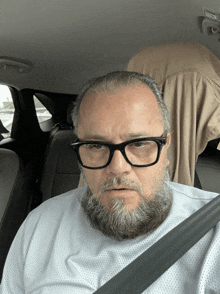 a man with glasses and a beard is sitting in the back of a car