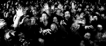 a black and white photo of a crowd of zombies reaching out their hands .