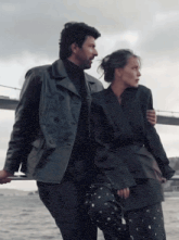 a man and a woman are standing next to each other in front of a bridge