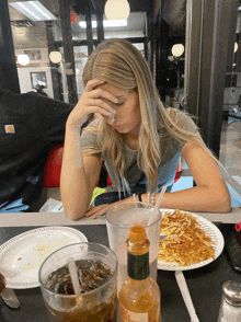 a woman sitting at a table with a plate of food and a glass of soda