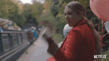 a woman in a red coat is reading a book while holding balloons and a sign that says netflix on it