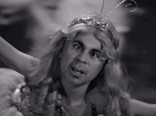 a black and white photo of a man wearing a wig and a crown on his head .