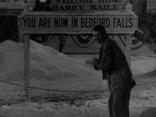 a black and white photo of a man standing in front of a sign that says `` you are welcome '' .