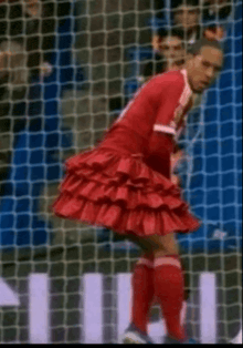 a soccer player wearing a red ruffled skirt is standing in front of a net