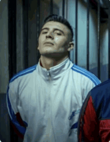 a man in a white and blue adidas jacket is standing in a dark room