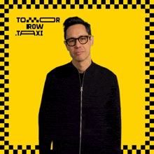 a man wearing glasses and a black jacket stands in front of a yellow and black checkered frame that says tomorrow row taxi