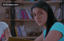 a woman in a blue shirt is sitting at a table in front of a bookshelf in a library .