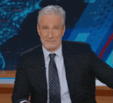 a man in a suit and tie is sitting in front of a screen
