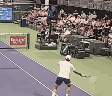 a man is holding a tennis racquet on a tennis court in front of an emirates fly better sign .