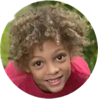 a young boy with curly hair is smiling in a pink shirt