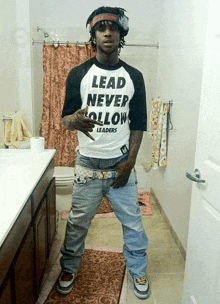 a man wearing a shirt that says lead never follow leaders is standing in a bathroom