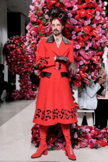 a man wearing a red coat and boots is standing in front of a bunch of flowers