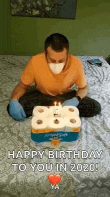 a man wearing a mask and gloves is sitting on a bed with a birthday cake made of toilet paper rolls .