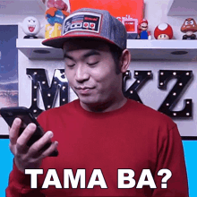 a man wearing a baseball cap is holding a cell phone and says tama ba