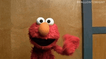 elmo from sesame street is standing in front of a wooden door and waving .