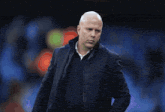 a bald man in a suit stands in front of a crowd watching a soccer match