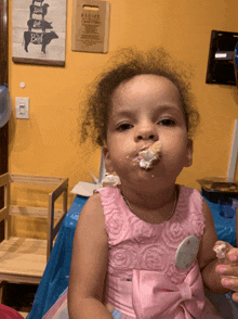 a little girl wearing a pink dress with a bow on it is eating cake