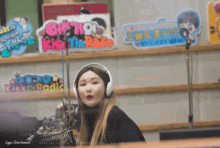 a woman wearing headphones stands in front of a microphone in a room with a sign that says kiss the radio