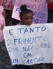 a little girl is holding a sign that says " e tanto sofrimento que não cabe em um cartaz "