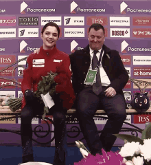 a man and a woman are sitting on a bench in front of a purple wall with tess logos on it