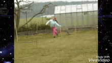 a girl in pink pants and a blue sweater is running in a field with a greenhouse in the background