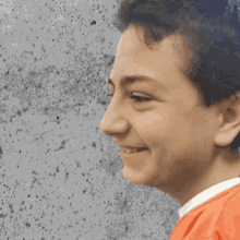 a young boy in an orange shirt is smiling in front of a gray wall