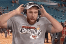 a man wearing a super bowl champions shirt and headphones is standing in a stadium with his hands on his head .