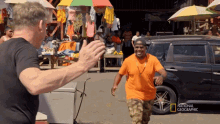 a man in an orange shirt is being greeted by a man in a black shirt with the words national geographic on the bottom