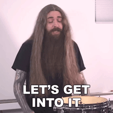 a man with long hair and a beard is playing a drum set and says let 's get into it