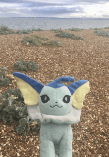 a stuffed animal is standing on a gravel beach