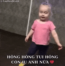 a little girl in a pink shirt is dancing in front of a wall