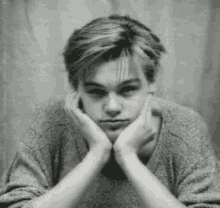 a young man is sitting down with his hands on his face .