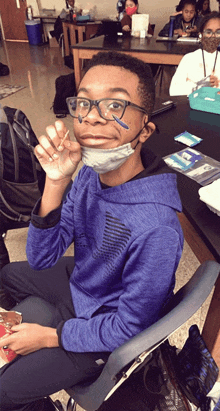 a young boy wearing glasses and a mask is sitting in a classroom