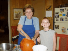 a woman in a blue apron is carving a pumpkin while a boy looks on