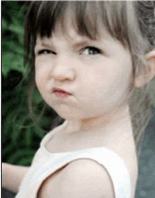 a little girl wearing a white tank top is making a funny face