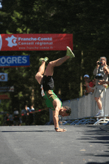 a man is doing a handstand in front of a sign that says franche-comte