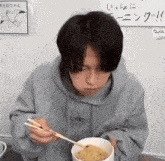 a man is eating a bowl of food with chopsticks .